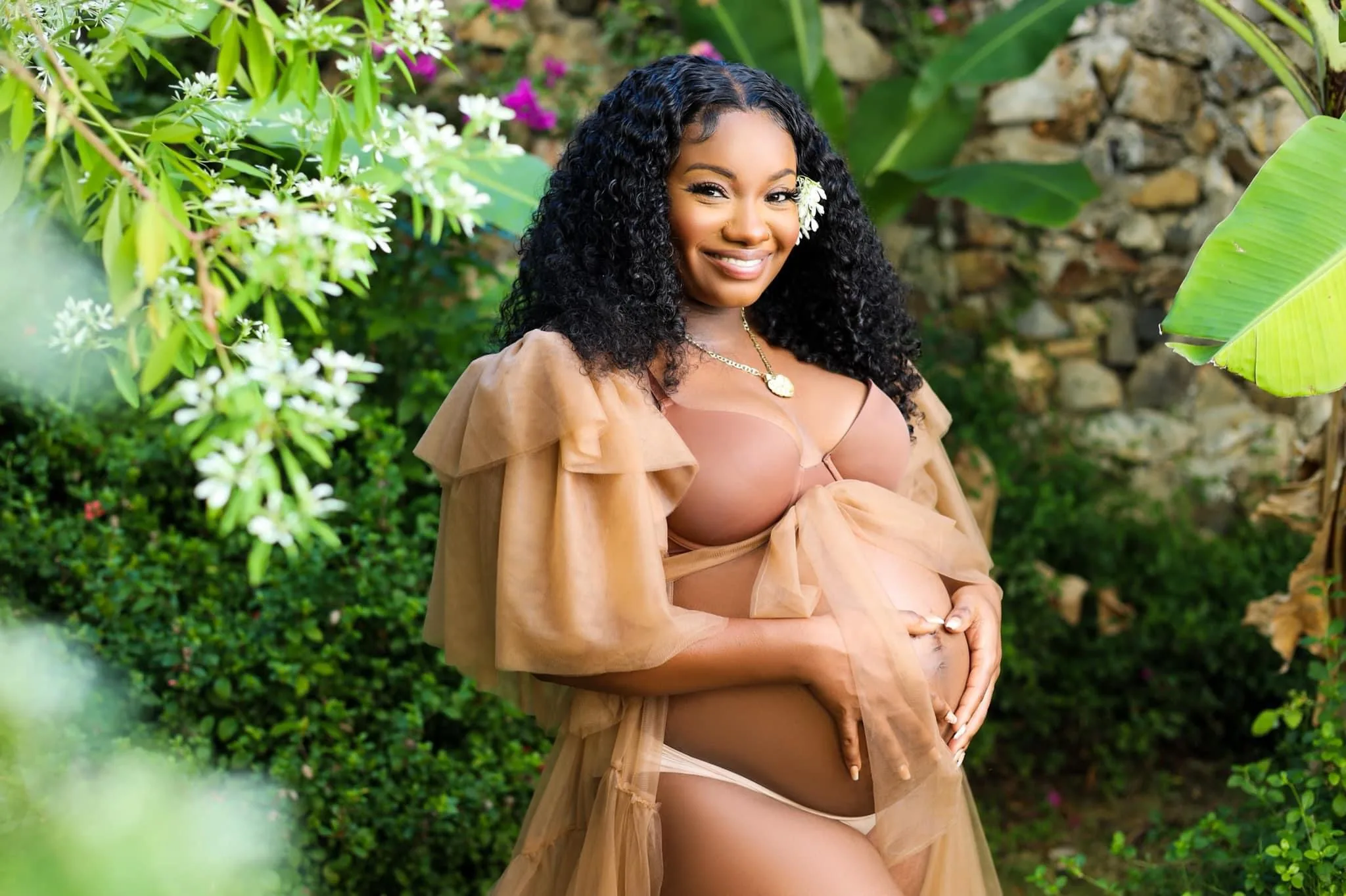 Maternity portrait of a smiling woman cradling her pregnant belly in a lush garden